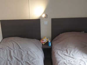A hotel room with two beds, a nightstand, and a wall-mounted light. - AC mobile home - 6 guests (Saint-Maime)