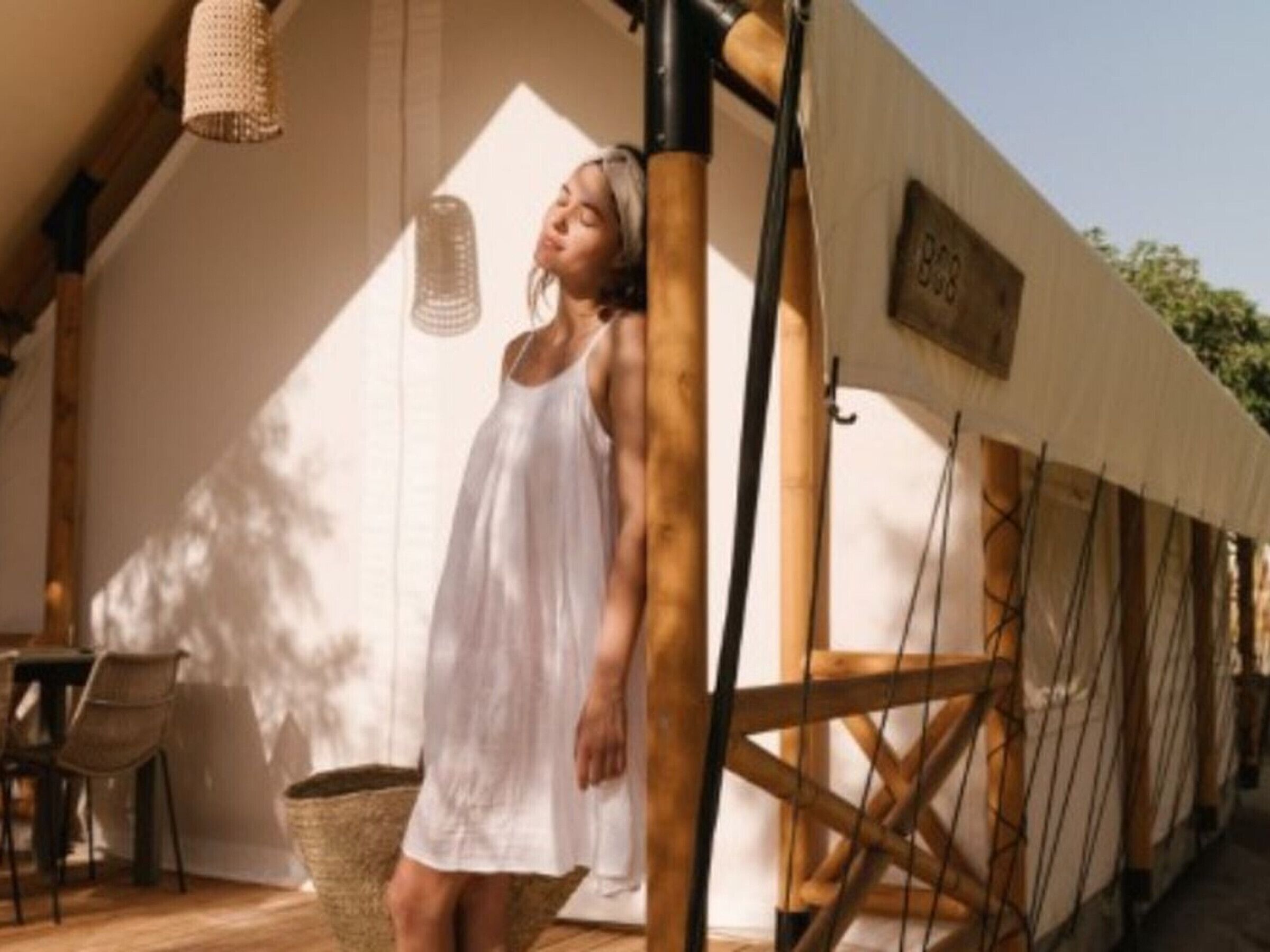 A person in a white dress standing near a bamboo structure, with a wicker basket and a table in the background.