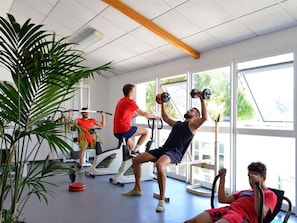 Une salle de sport équipée de matériel d’exercice, dotée de grandes fenêtres et agrémentée de plantes d’intérieur.