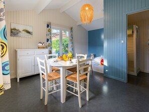 A dining area with a white table and chairs, a hanging light fixture, and a view of the outdoors. - Cozy chalet, pets friendly - 4 guests (Saint-Jean-de-Monts)
