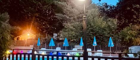 Zona de piscina con valla, sombrillas y una mesa con sillas.