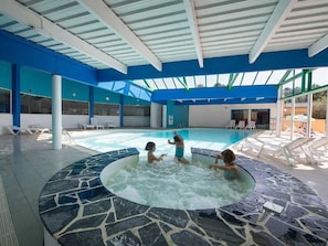 A swimming pool area with a hot tub, lounge chairs, and a covered roof structure.