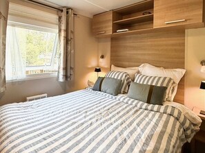A bedroom with a bed, curtains, a bedside table, and a built-in shelf. - Mobile home, AC, pets OK - 6 guests (Saint-Hilaire-de-Riez)