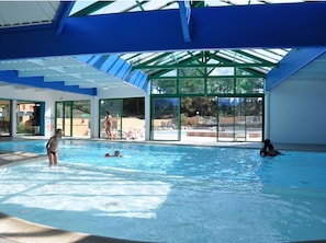 An indoor swimming pool with clear glass walls, a blue roof, and a poolside area visible through the glass. - Mobile home, AC, pets OK - 6 guests (Saint-Hilaire-de-Riez)