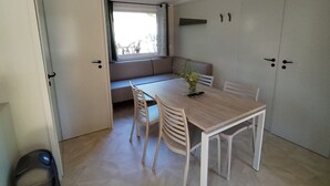 A room with a dining table, chairs, a bench, a window with curtains, and a wardrobe. - Mobile home, pets welcome - 4 guests (Chaillé-les-Marais)