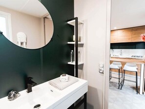 Ein modernes Badezimmer mit einem weißen Waschtisch, einem runden Spiegel und einer dunkelgrünen Akzentwand.