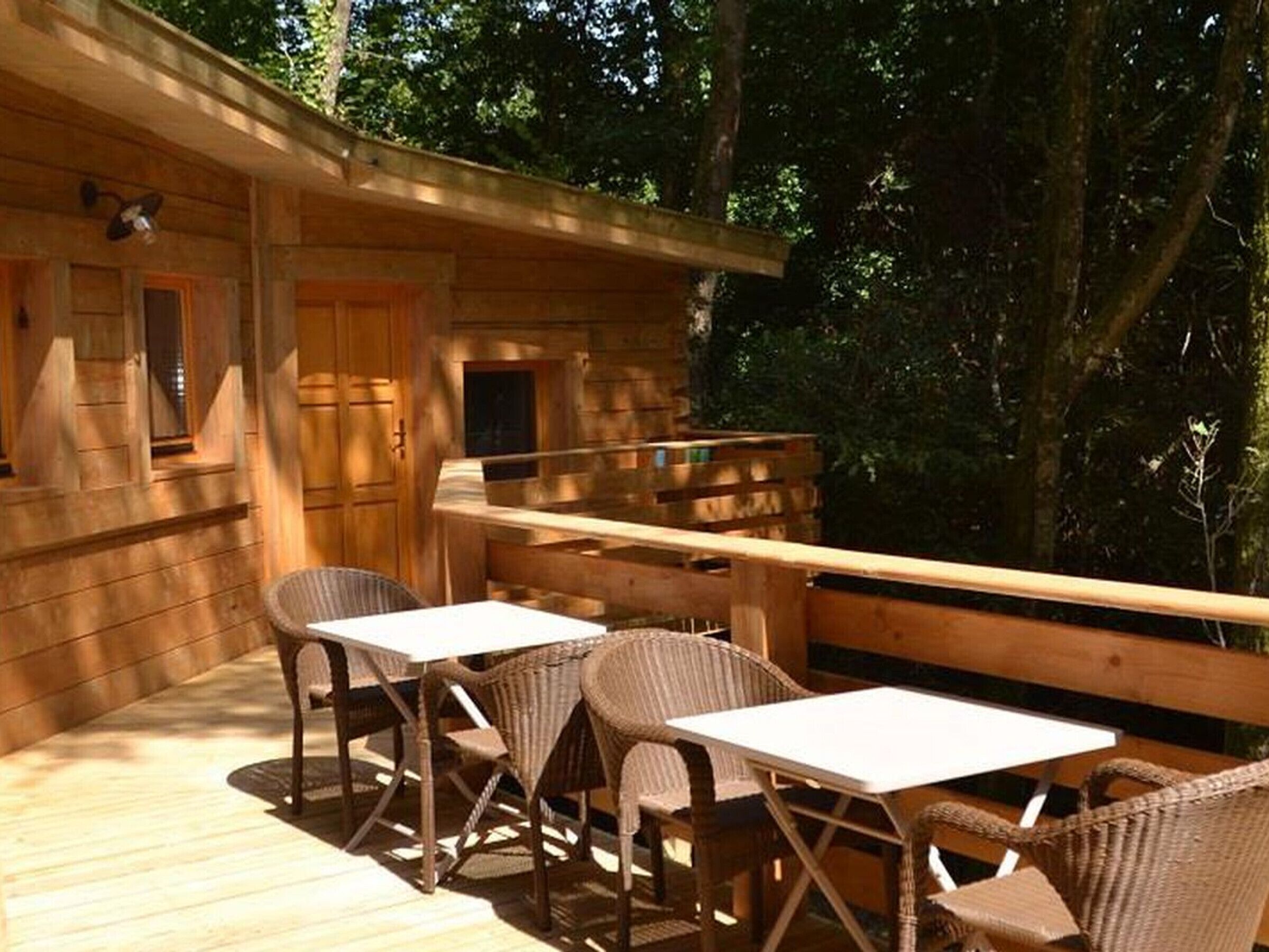 Una cabaña de madera con terraza, dos mesas y cuatro sillas de mimbre.