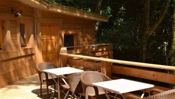 Una cabaña de madera con terraza, dos mesas y cuatro sillas de mimbre.