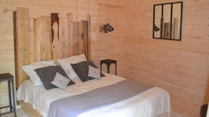 A wooden cabin bedroom with a bed, pillows, a nightstand, a lamp, and a mirror on the wall. - Chalet with disabled access - 6 guests (Magné)