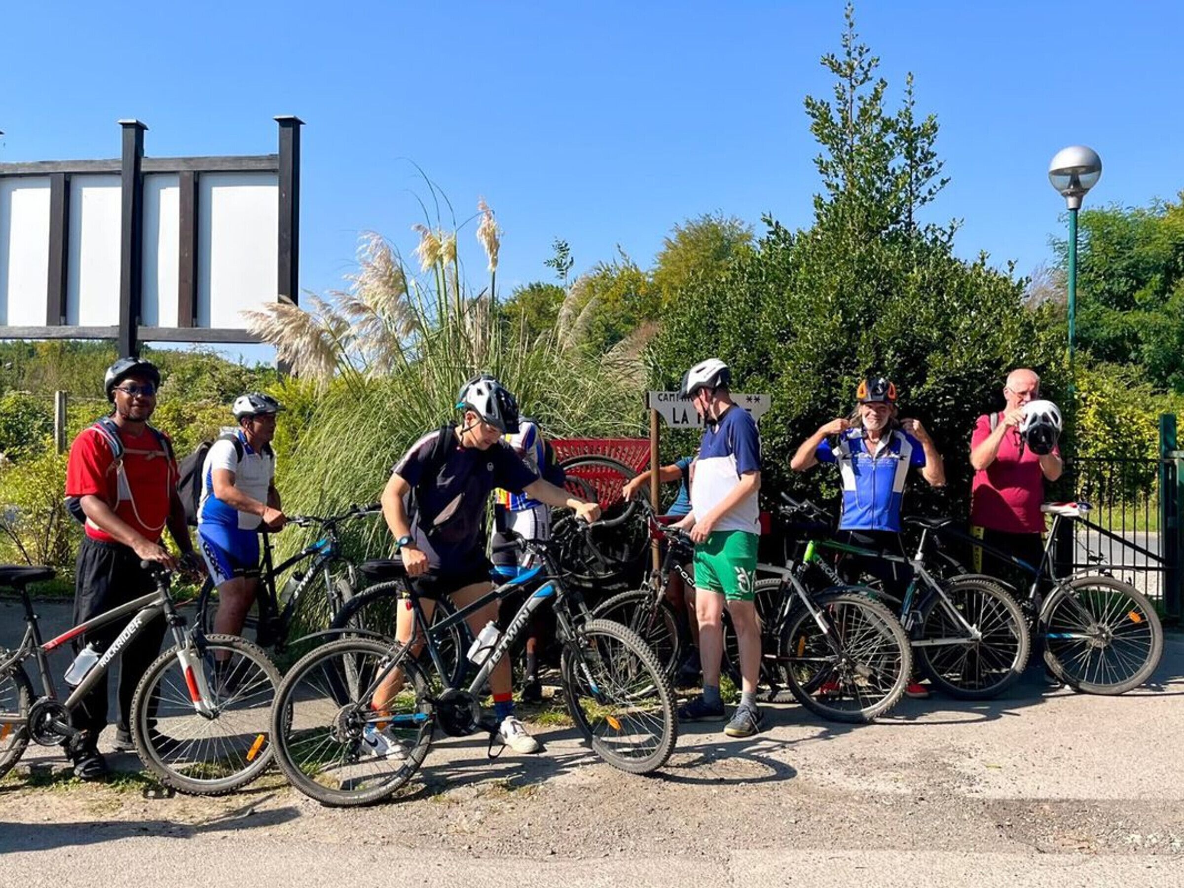 Un groupe de cyclistes s’est rassemblé autour de vélos dans un cadre extérieur, au milieu de la verdure, sous un ciel dégagé.