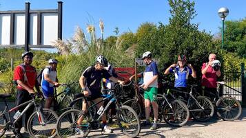 Un groupe de cyclistes s’est rassemblé autour de vélos dans un cadre extérieur, au milieu de la verdure, sous un ciel dégagé.