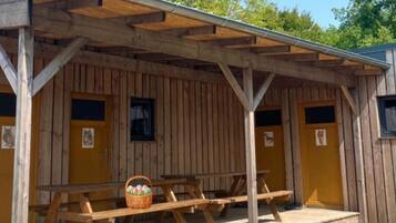 A wooden cabin with a covered porch, picnic tables, and yellow doors.
