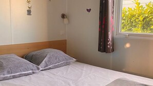 Un letto con cuscini, una lampada da comodino, un addobbo a parete e una finestra con tende.