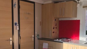 Una cucina compatta con mobili in legno, un frigorifero rosso e un piccolo lavandino.