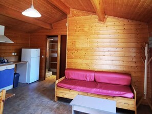 Interior de una cabaña de madera con kitchenette, un sofá y una mesa de comedor.