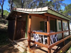 Una pequeña cabaña de madera con un porche, sillas de plástico blanco y una terraza de madera.