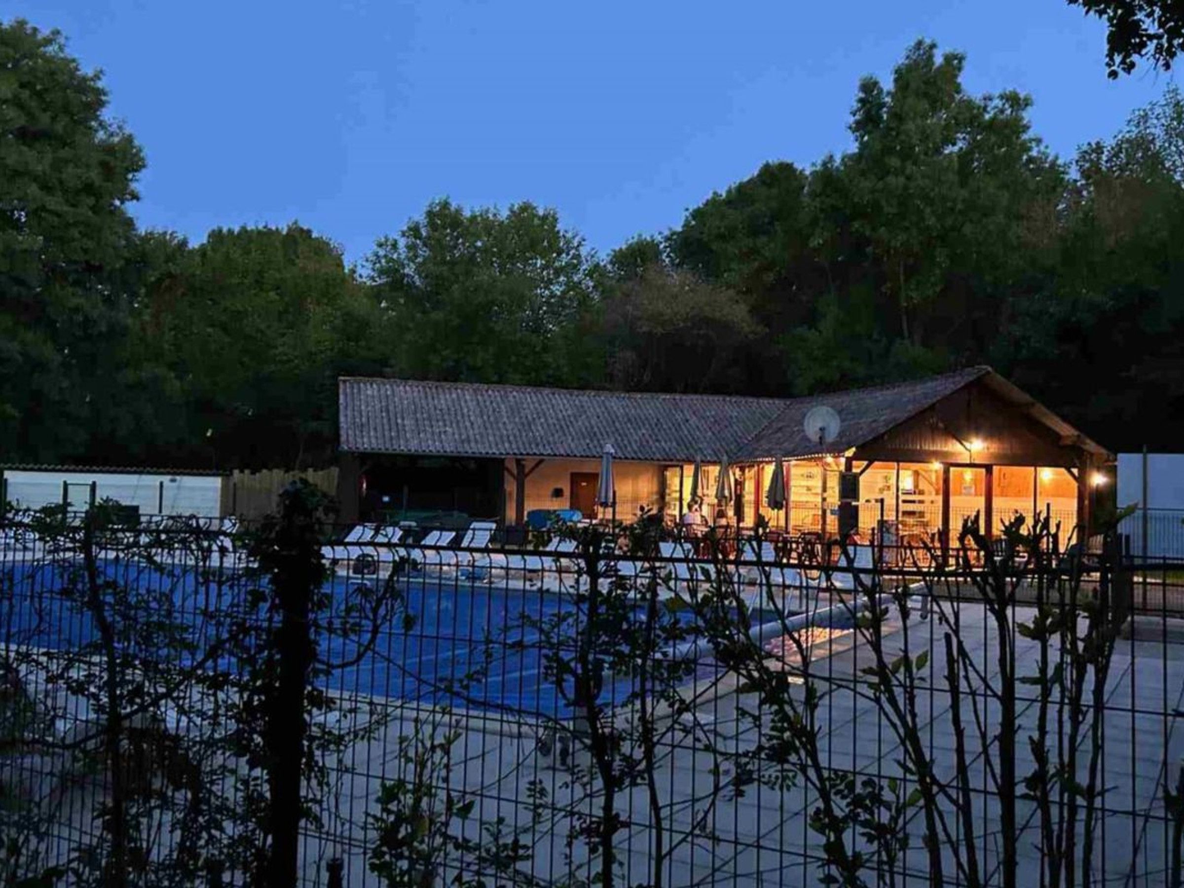 A poolside building with a tiled roof, surrounded by a fence and trees.