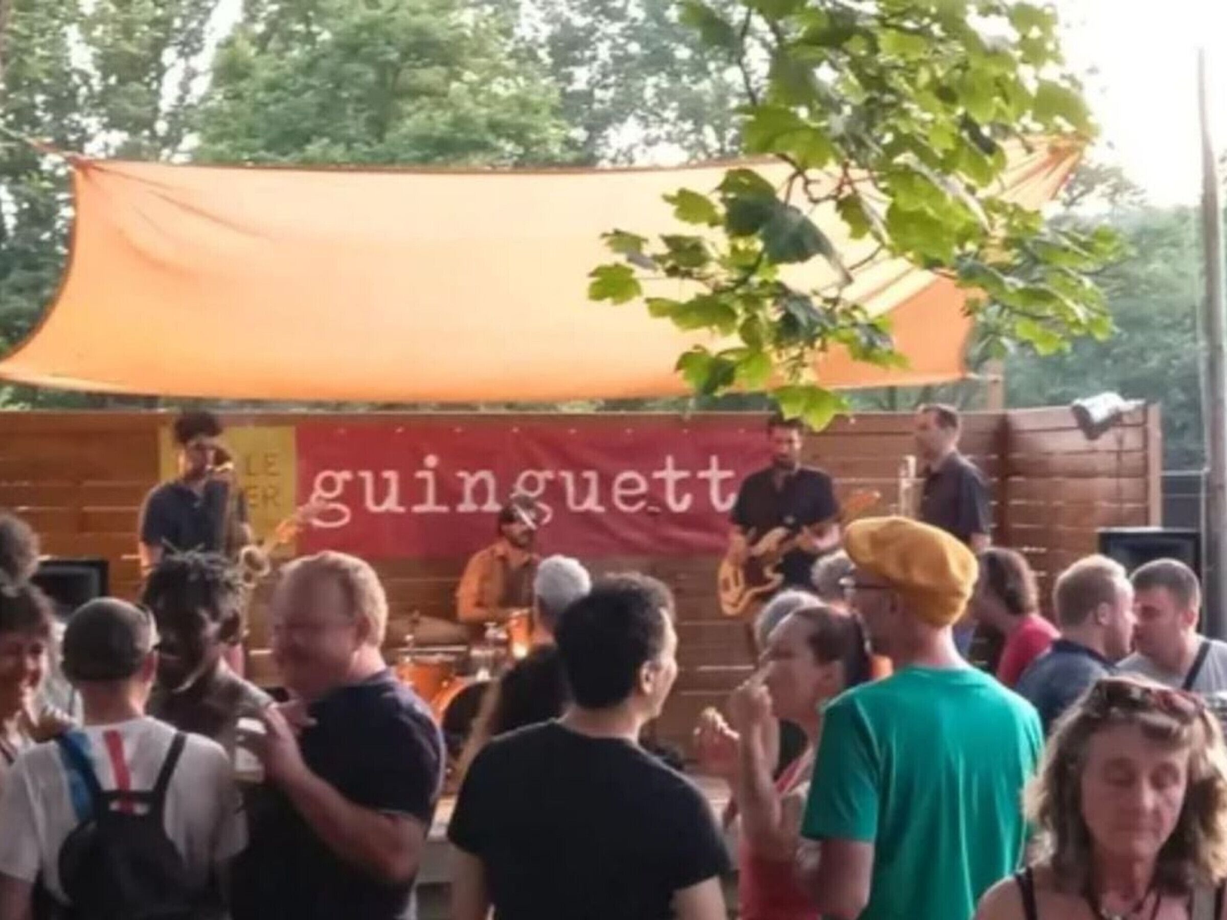 A crowded outdoor event with a stage and a banner.