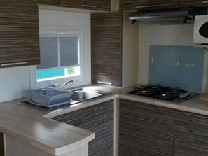 A modern kitchen with a built-in gas stove, a sink, and a window with blinds. - Mobile home pets allowed - 4 guests (Perros-Guirec)