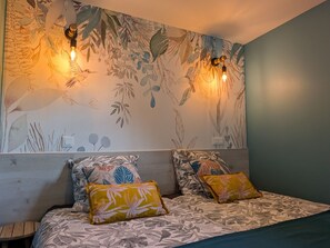 Une chambre à coucher avec un papier peint à motifs floraux, deux lampes fixées au mur et un lit avec une literie et des oreillers à motifs.