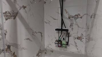 Une salle de bain aux murs de marbre et dotée d’un porte-serviettes noir où sont rangés les articles de toilette.