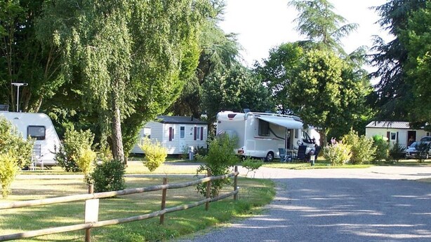 Ein Campingplatz mit Wohnmobilen und Wohnwagen, einem Kiesweg und einem Holzzaun.