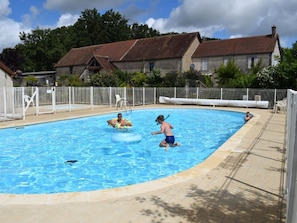 Ein Schwimmbecken mit gefliestem Sonnendeck, einem weißen Zaun und Häusern im Hintergrund.