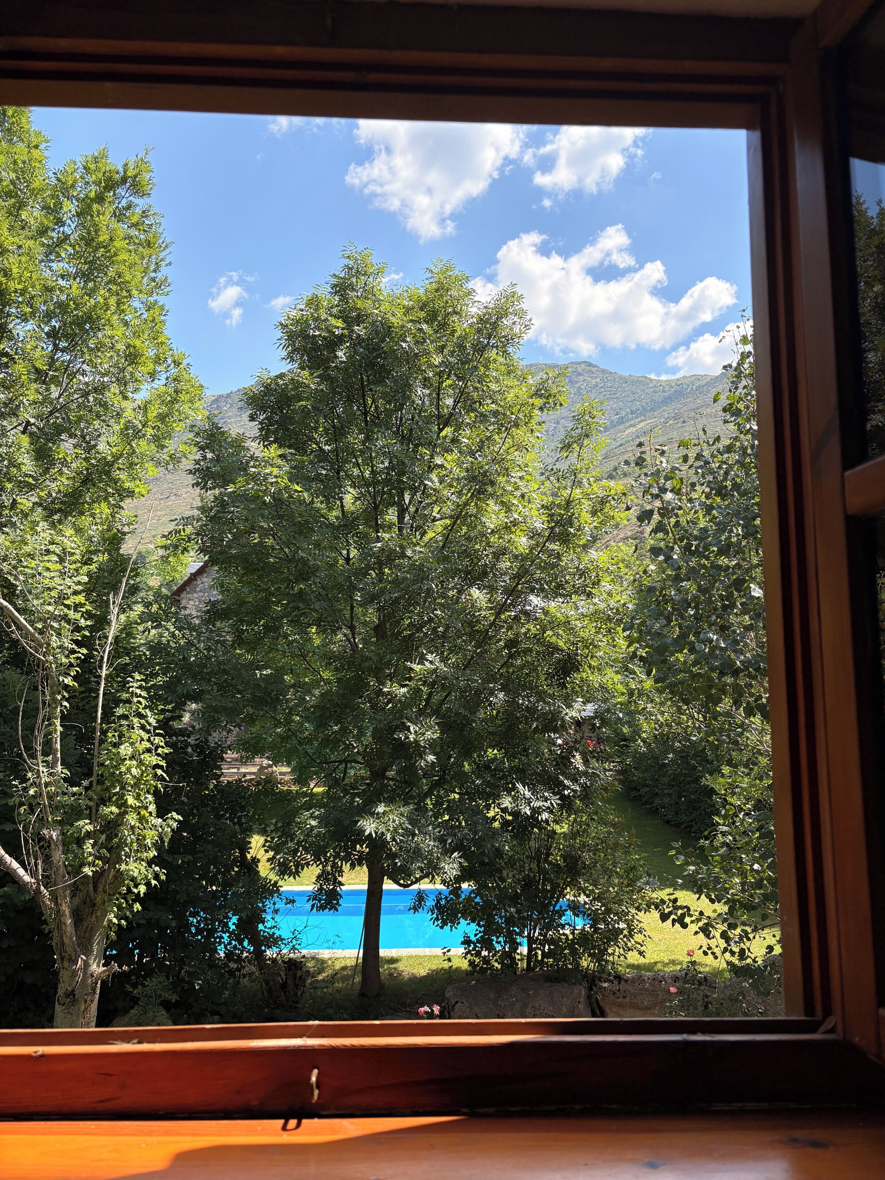 A window view of a mountainous landscape with trees and a blue body of water.