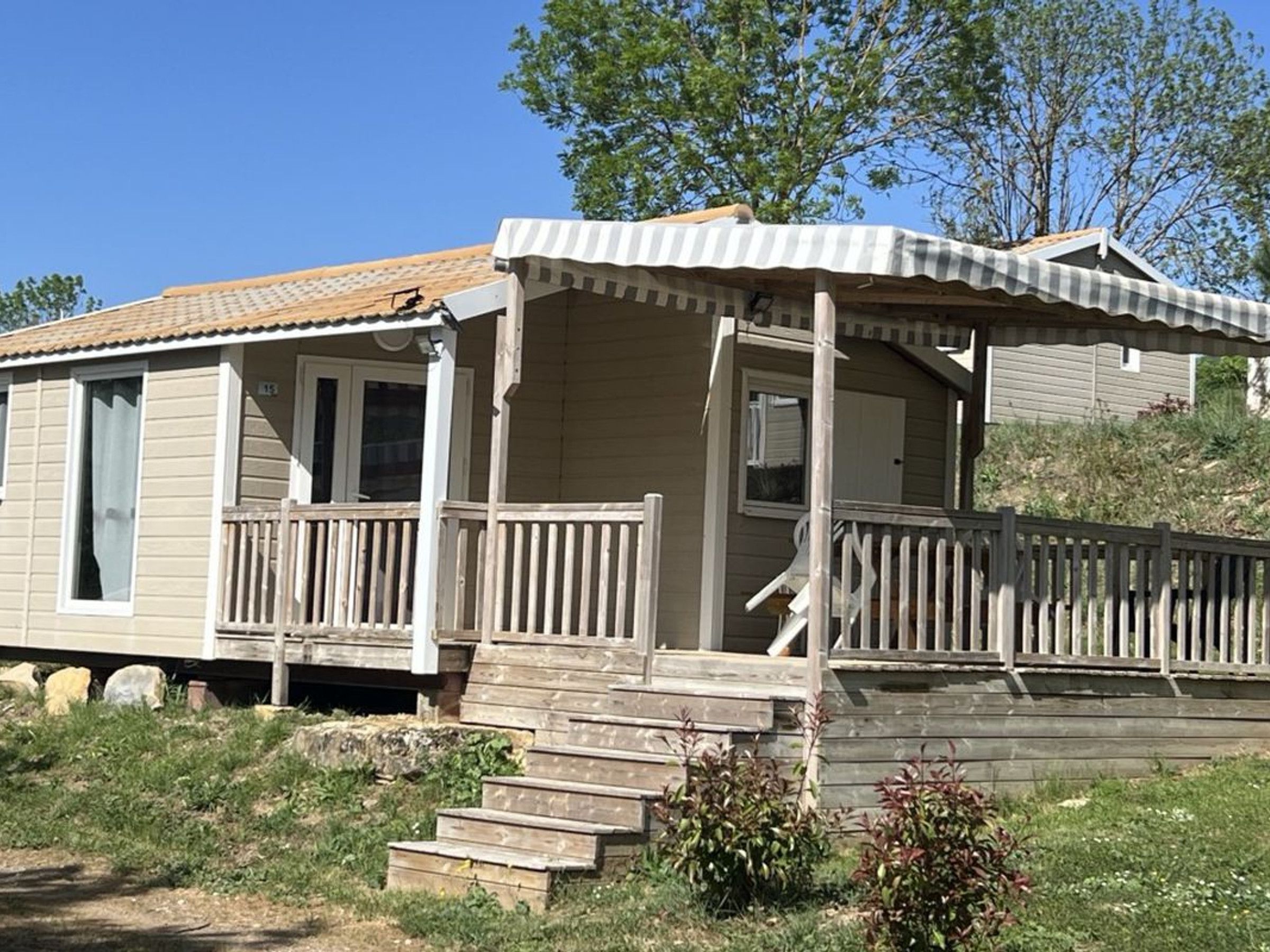 Une maison mobile dotée d’une véranda, d’un escalier en bois et d’un petit jardin.