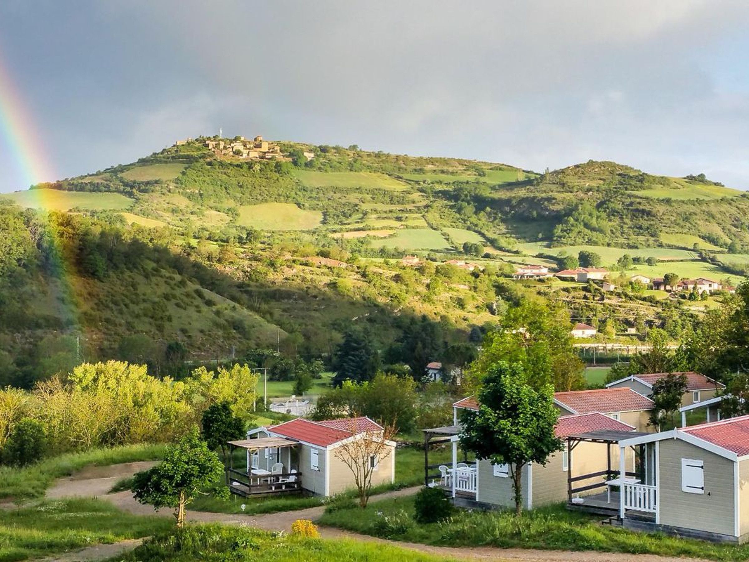 Un paisaje rural con una colina, un arcoíris y un grupo de casas pequeñas con tejados rojos.