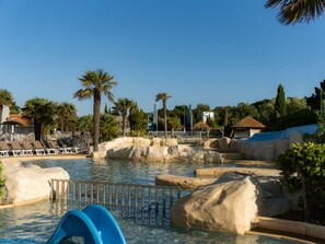 Zona de piscina con agua cristalina, palmeras y sillas de descanso.