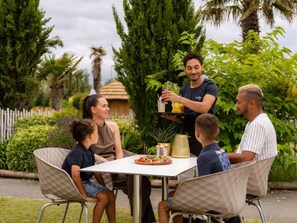Un grupo de personas sentadas alrededor de una mesa al aire libre, mientras un camarero sirve bebidas.