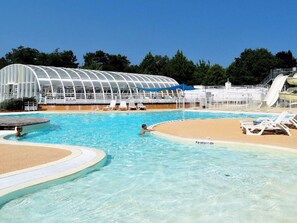 Una piscina con zona arenosa, sillas de descanso, una estructura cubierta y un tobogán de agua.