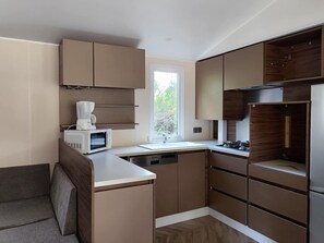 A compact kitchen with built-in appliances, a window, and a view of greenery. - Mobile home, pets welcome - 6 guests (La Tour-d'Auvergne)