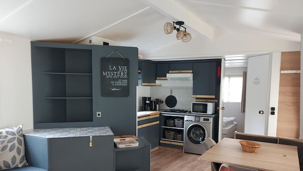 Een praktische keuken met een magnetron, fornuis en wasmachine, een eethoek met een tafel en stoelen, en een ingebouwde zithoek met een bank en een wandplank.