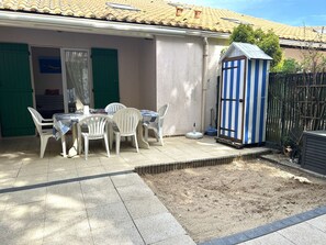 Eine Terrasse mit Tisch und Stühlen, eine kleine Gartenhütte und ein umzäunter Gartenbereich.