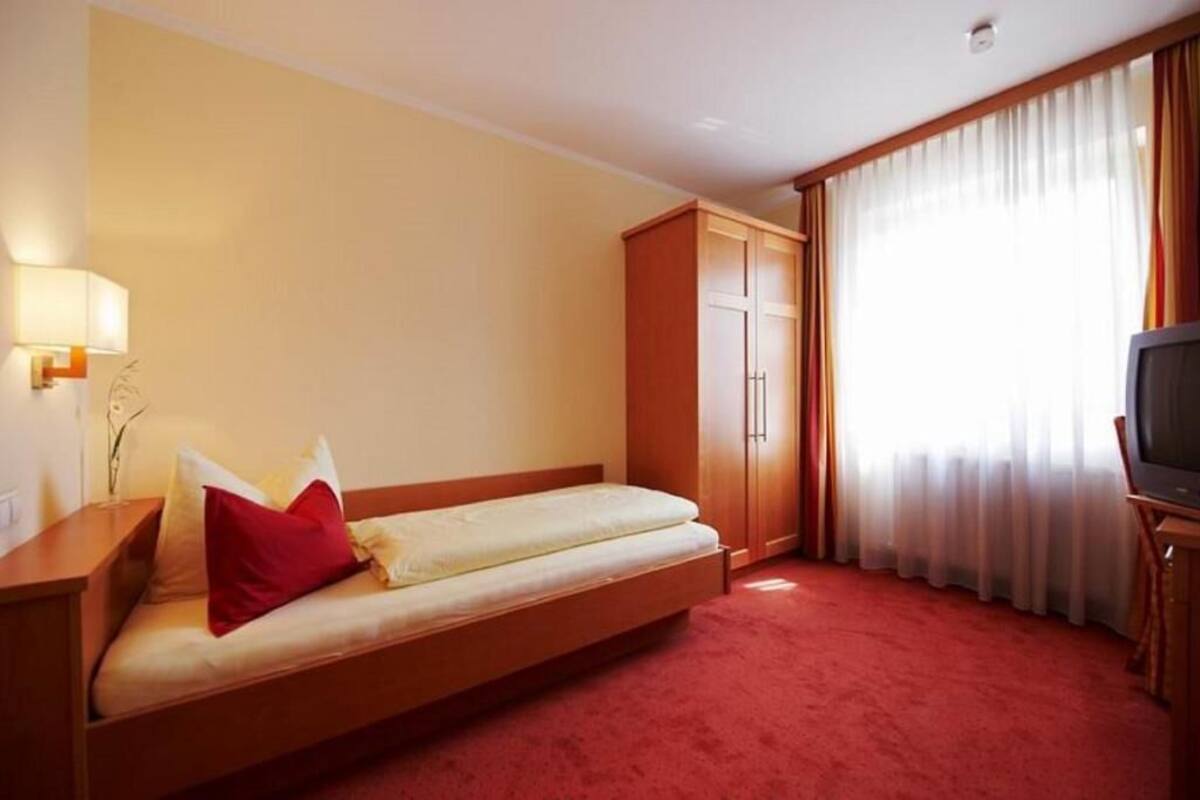 A hotel room with a single bed, a wardrobe, a television, and a lamp.