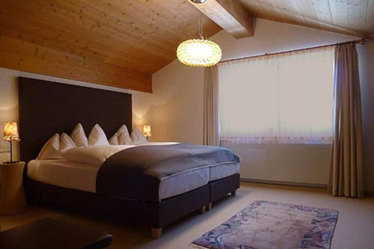 A bedroom with a bed, bedside lamps, a rug, and a window with curtains.