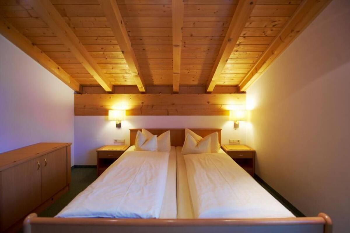 A room with a wooden ceiling, two beds, bedside lamps, and a wooden cabinet.