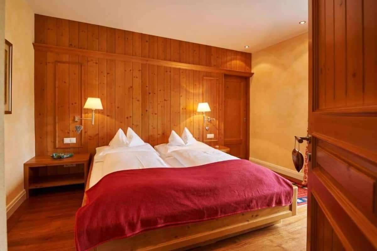 A wooden-paneled bedroom with a bed, two bedside lamps, and a nightstand.