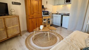 A compact living space with a kitchenette, a television on a cabinet, a dining area with a table and chairs, and a sofa. - Loft studio, AC & pool - 2 adults, 2 kids (Gruissan)