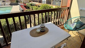 A balcony with a table, a chair, and a view of a swimming pool and neighboring buildings. - Loft studio, AC & pool - 2 adults, 2 kids (Gruissan)
