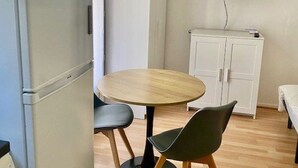 Et lille værelse med et rundt træbord, to stole, et hvidt skab, en hvid garderobe og et fladskærms-TV ophængt på væggen.