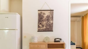Een kamer met een witte koelkast, een aan de muur hangend schilderij, een houten kast en een telefoon.