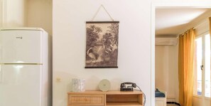 A room with a white refrigerator, a wall-mounted picture, a wooden cabinet, and a telephone. - Apartment, pets welcome - 3 guests, pine view (Le Lavandou)