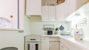 Een keuken met witte kastjes, een fornuis, een spoelbak en een aanrecht met een koffieapparaat en een tas boodschappen.
