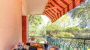Een balkon met uitzicht op bomen, een tafel met ontbijtartikelen en een rode luifel.