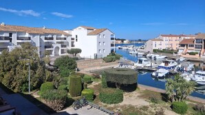 Puerto deportivo con barcos, edificios blancos con balcones y abundante vegetación.