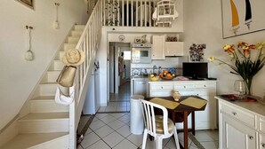 Una cocina con armarios blancos, una mesa de comedor con sillas, un televisor y una escalera con jaula colgante.