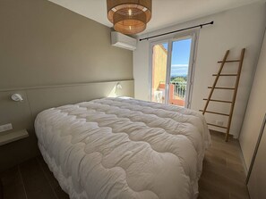A bedroom with a large bed, a ceiling fan, a window with a view, and a wooden ladder. - 2-bedroom house with garden and sea view in La Croix-Valmer (La Croix-Valmer)